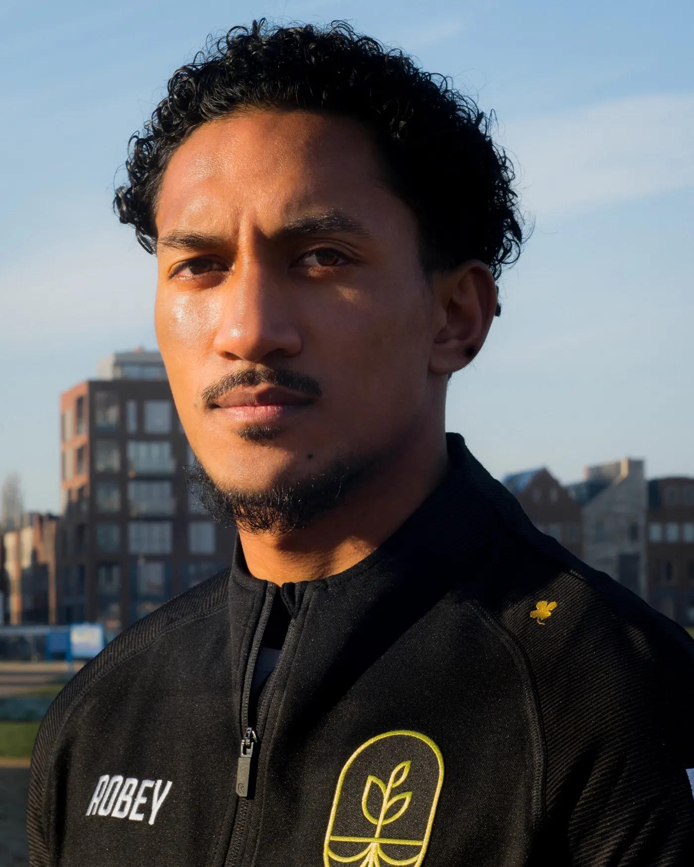 Tapmahoe Sopacua in een zwart Voetbal Dream Coach trainingsjack, buiten in de zon