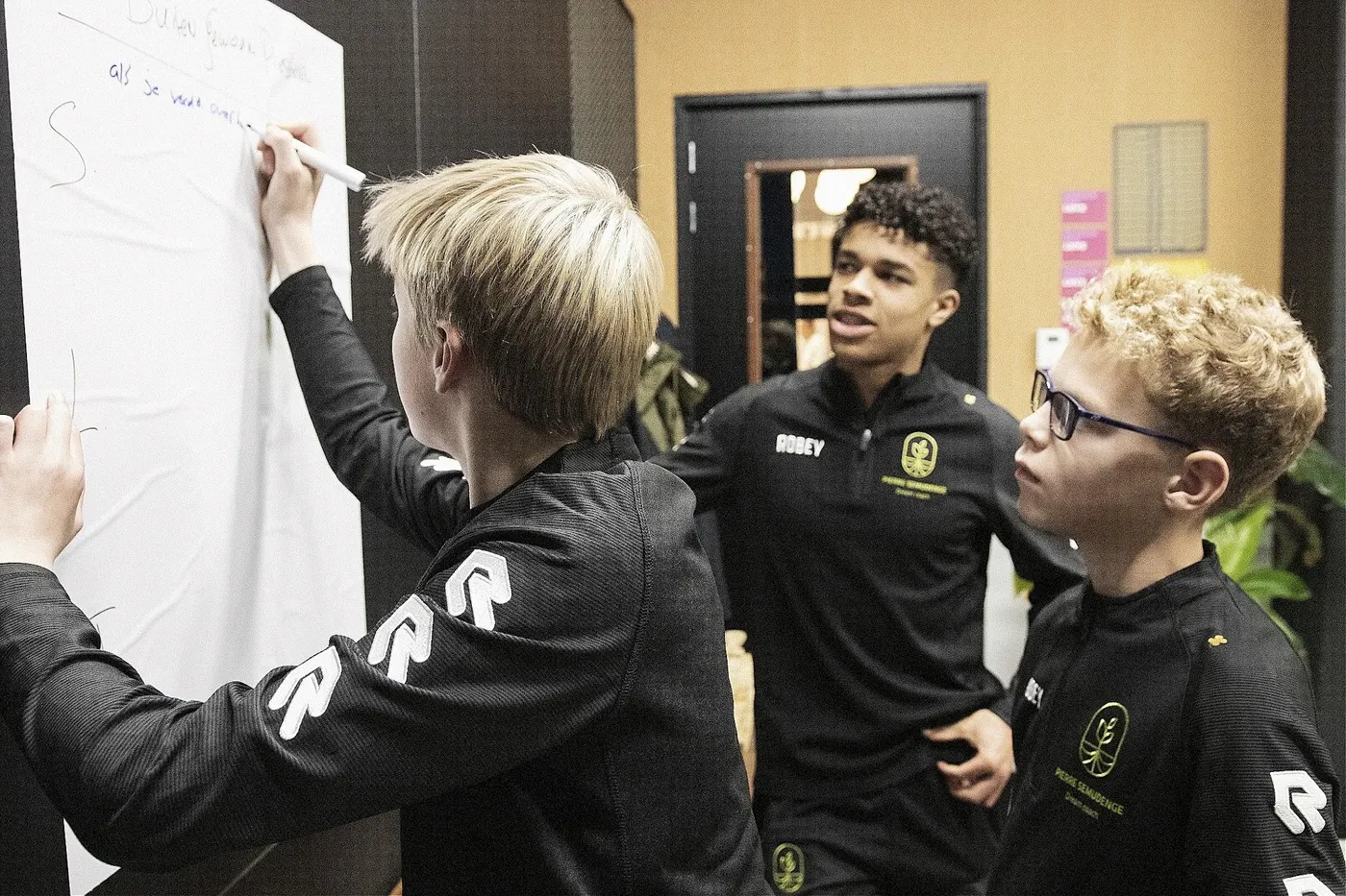 Jeugdspelers schrijven mee op een flip-over tijdens een sessie